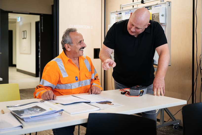 Two electrical workers, one at a desk with reference materials