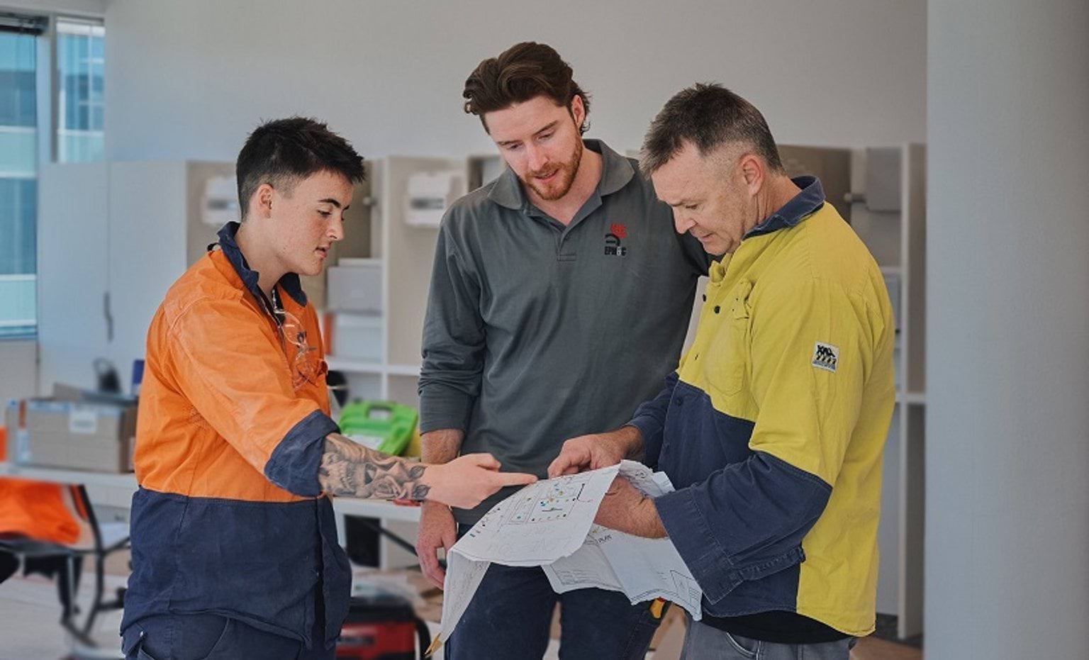 Two apprentice electricians at work with their supervisor discussing plans