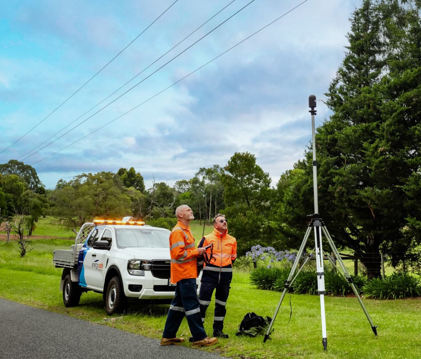 Two line clearance professionals inspect power lines in a rural setting.