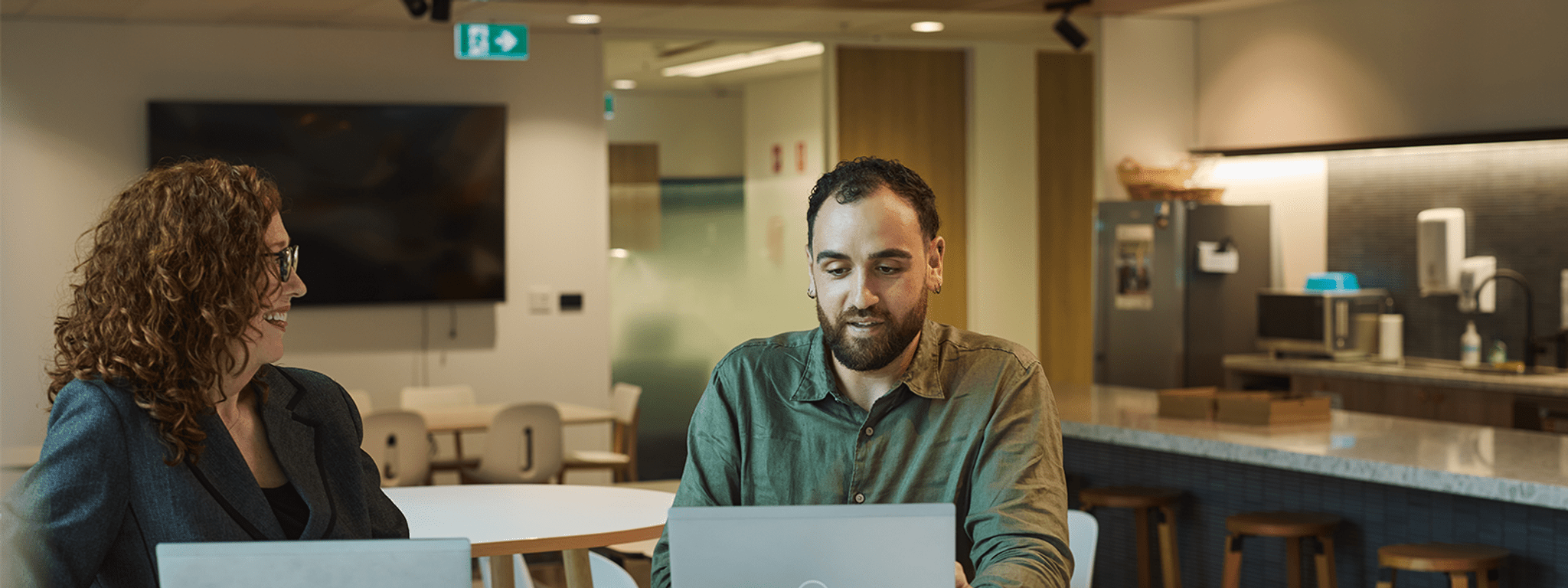 Two Energy Safe employees sitting at a table with open laptops engaged in a collaborative discussion.